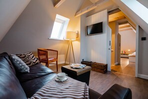 A cozy loft bedroom with a sloped ceiling, a large window, a flat-screen TV, a wooden chair, a small table with a cup and saucer, and a striped throw blanket. - Seaside Lodge Sylt with sauna - Welcome to the luxury vacation home (Sylt)