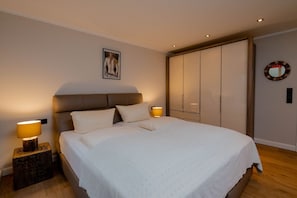 A neatly arranged bedroom with a large bed, two bedside lamps, a framed artwork on the wall, and a wardrobe. - Seaside Lodge Sylt with sauna - Welcome to the luxury vacation home (Sylt)