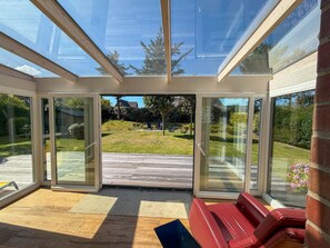 A conservatory with a glass roof, sliding glass doors, and a red bench. - Beachfront Lodge on Sylt with Sauna - Welcome to the Luxury Vacation Home (Sylt)
