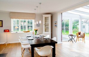 A dining area with a dark wooden table, white chairs, and a glass cabinet.