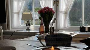 Una stanza con un tavolo apparecchiato per mangiare, un vaso di fiori, una bottiglia e una radio sul davanzale.