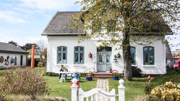 Una casa bianca con tetto grigio, una porta blu e un recinto di legno bianco.