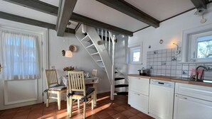 Una cucina con zona pranzo, mobili bianchi, schienale piastrellato e una scala in legno.