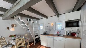 Una cucina compatta con mobili bianchi, un piano di lavoro in legno, un forno a microonde integrato e un piccolo oblò.