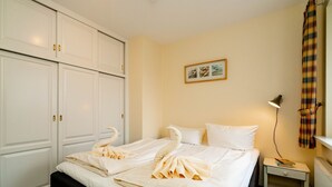 A hotel room with a bed, a nightstand, a lamp, a wardrobe, and a framed picture on the wall. - Godewind ground floor - Moin Moin and welcome to the ground floor 3-room (Sylt-Ost)