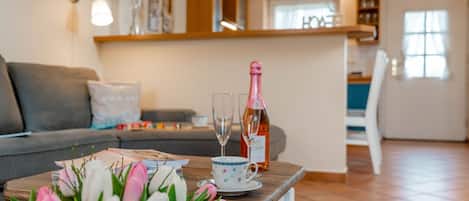 A living room with a wooden coffee table, a vase of tulips, a bottle of champagne, and a glass.