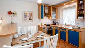 A modern kitchen with wooden cabinets, a dining table set for four, and a window with curtains. - Godewind ground floor - Moin Moin and welcome to the ground floor 3-room (Sylt-Ost)