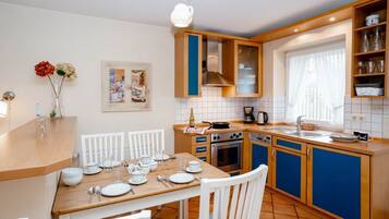 A modern kitchen with wooden cabinets, a dining table set for four, and a window with curtains.