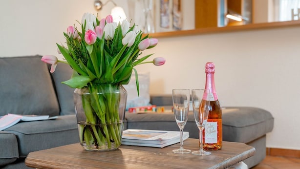 A living room with a grey sofa, a glass vase with tulips, two wine glasses, and a bottle of champagne on a wooden table. - Godewind ground floor - Moin Moin and welcome to the ground floor 3-room (Sylt-Ost)