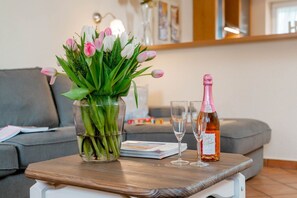 A living room with a grey sofa, a glass vase with tulips, two wine glasses, and a bottle of champagne on a wooden table. - Godewind ground floor - Moin Moin and welcome to the ground floor 3-room (Sylt-Ost)