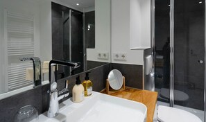 Une salle de bain moderne avec un grand miroir, un lavabo blanc et une cabine de douche en verre.