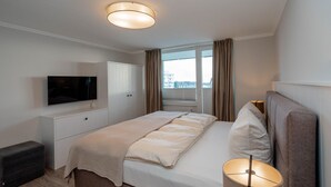 Een moderne hotelkamer met een groot bed, een flatscreen televisie aan de muur, een nachtkastje met een lamp en een raam met gordijnen.