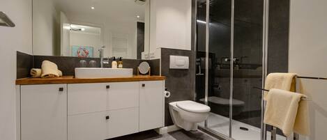 Un baño moderno con un espejo grande, un lavabo, un inodoro y una ducha con mampara de vidrio.