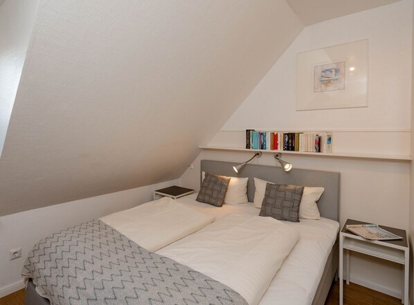 A bedroom with a bed, two bedside tables, a shelf with books, and a framed picture on the wall. - Dorothea, 1st Floor - Hello and welcome to the 3-room vacation apartment (Wenningstedt-Braderup (Sylt))