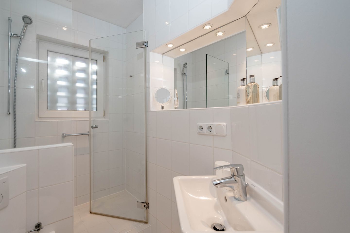 Une salle de bain moderne avec une douche en verre, un lavabo avec un miroir au-dessus et une fenêtre avec des stores.