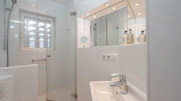 Une salle de bain moderne avec une douche en verre, un lavabo avec un miroir au-dessus et une fenêtre avec des stores.