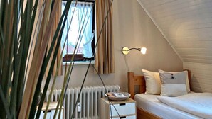 Une chambre confortable avec un plafond en pente, un lit, des lampes de chevet, un radiateur et une fenêtre avec des rideaux.