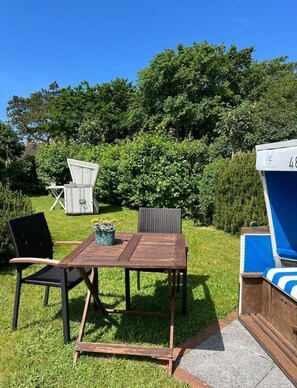 Un espace extérieur aménagé avec une table et des chaises en bois, entouré d’une végétation luxuriante et d’une haie.