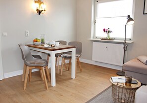 A modern dining area with a wooden table and chairs, a small side table with a lamp, and a window with flowers.