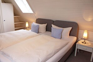 Une chambre à coucher avec un grand lit, deux tables de chevet avec des lampes, une armoire et une lucarne.