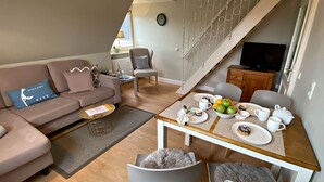 Un salon moderne avec un canapé, une table basse et une table à manger, cette dernière étant mise avec des assiettes, des tasses et des fruits.
