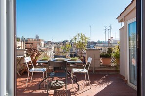 Une terrasse sur le toit, avec une table et des chaises, des plantes en pot et une vue sur le paysage urbain.