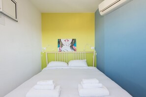 Un lit simple avec du linge de lit blanc, une tête de lit verte, un mur jaune et un mur bleu.