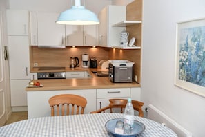 A compact kitchen with white cabinets, a wooden countertop, a coffee maker, a toaster, and a dining table with a checkered tablecloth.