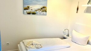 Een hotelkamer met een bed, een nachtkastje, een lamp, een schilderij van een strand en een blauw gordijn.