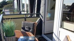 A balcony with a wooden table, a chair, a potted plant, and a door leading to an interior space.