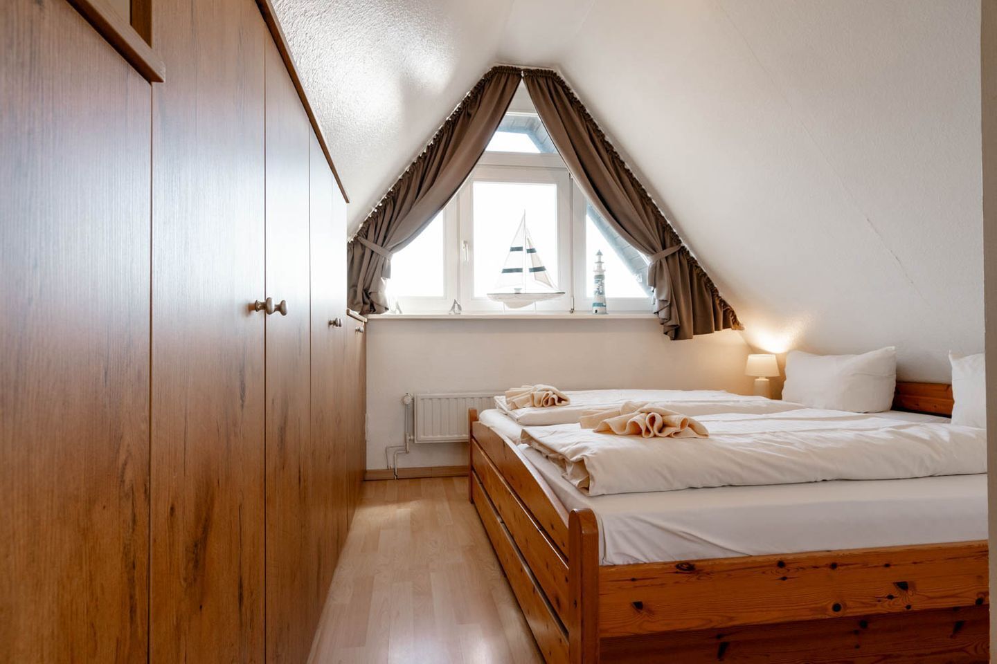 Une chambre à coucher avec un lit en bois, une fenêtre avec des rideaux, un radiateur et une armoire.