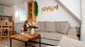 A living room with a beige sofa, a wooden coffee table with a vase of flowers, and a wall-mounted decoration.