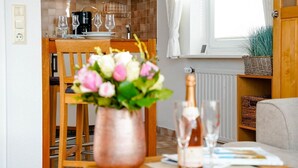 A dining area with a wooden table, chairs, a vase of flowers, and a bottle of champagne.