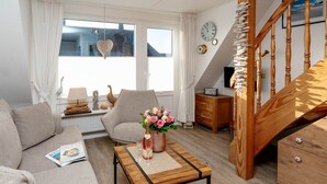 A cozy living room with a wooden staircase, a sofa, a coffee table with flowers, and a view of the outside.