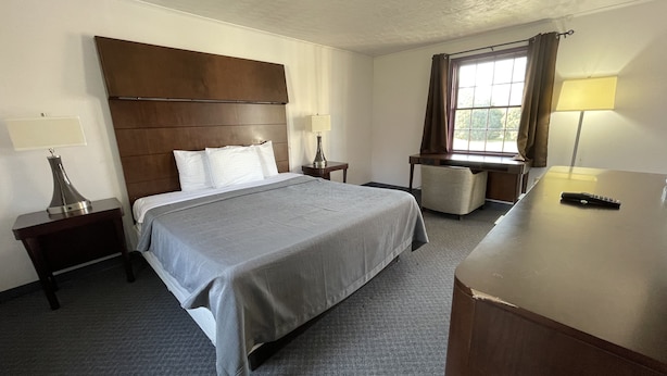 A hotel room with a large bed, a desk, a chair, and a window with curtains. - Rips Country Inn (Bowie)