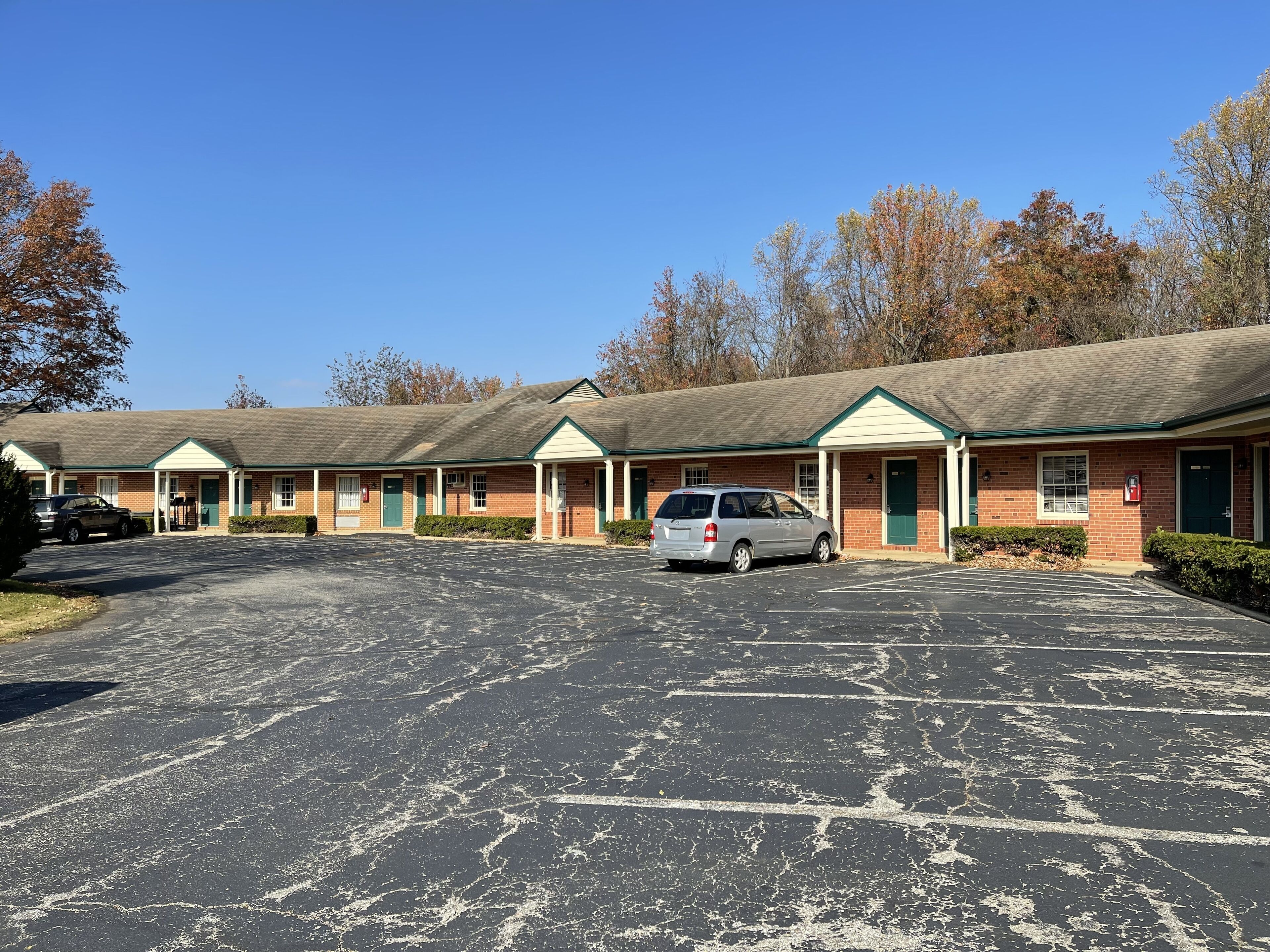 Un motel con varias habitaciones, un estacionamiento y un paisaje verde.