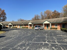 Un motel con varias habitaciones, un estacionamiento y un paisaje verde.