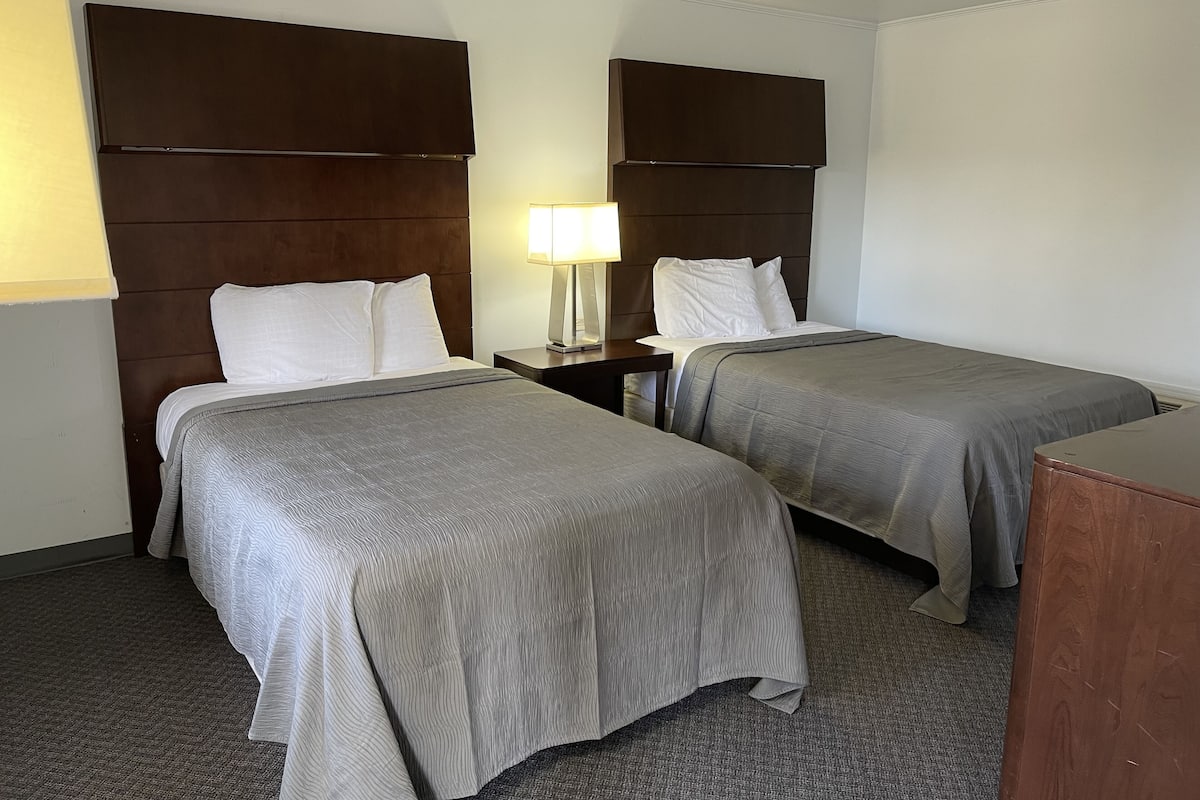 A hotel room with two beds, a nightstand with a lamp, and a wooden headboard.