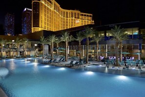 Ein Hotelpoolbereich mit Liegestühlen und Palmen, umgeben von modernen Gebäuden.