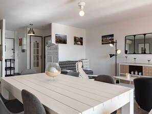 Un comedor moderno con una mesa blanca, sillas grises y un vaso de agua. Hay cuadros en la pared, un sofá blanco y negro y un aparador blanco con copas de vino.