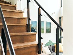 A staircase with wooden steps and black handrails, leading to a room with a view of mountains through a window.