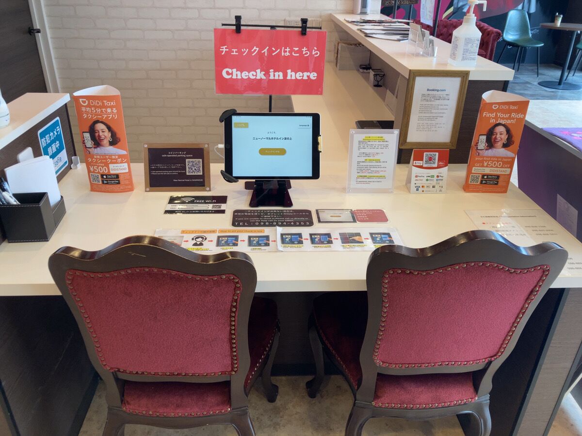 Un mostrador de recepción con una computadora, carteles informativos y un letrero que dice 'Registrarse aquí'.
