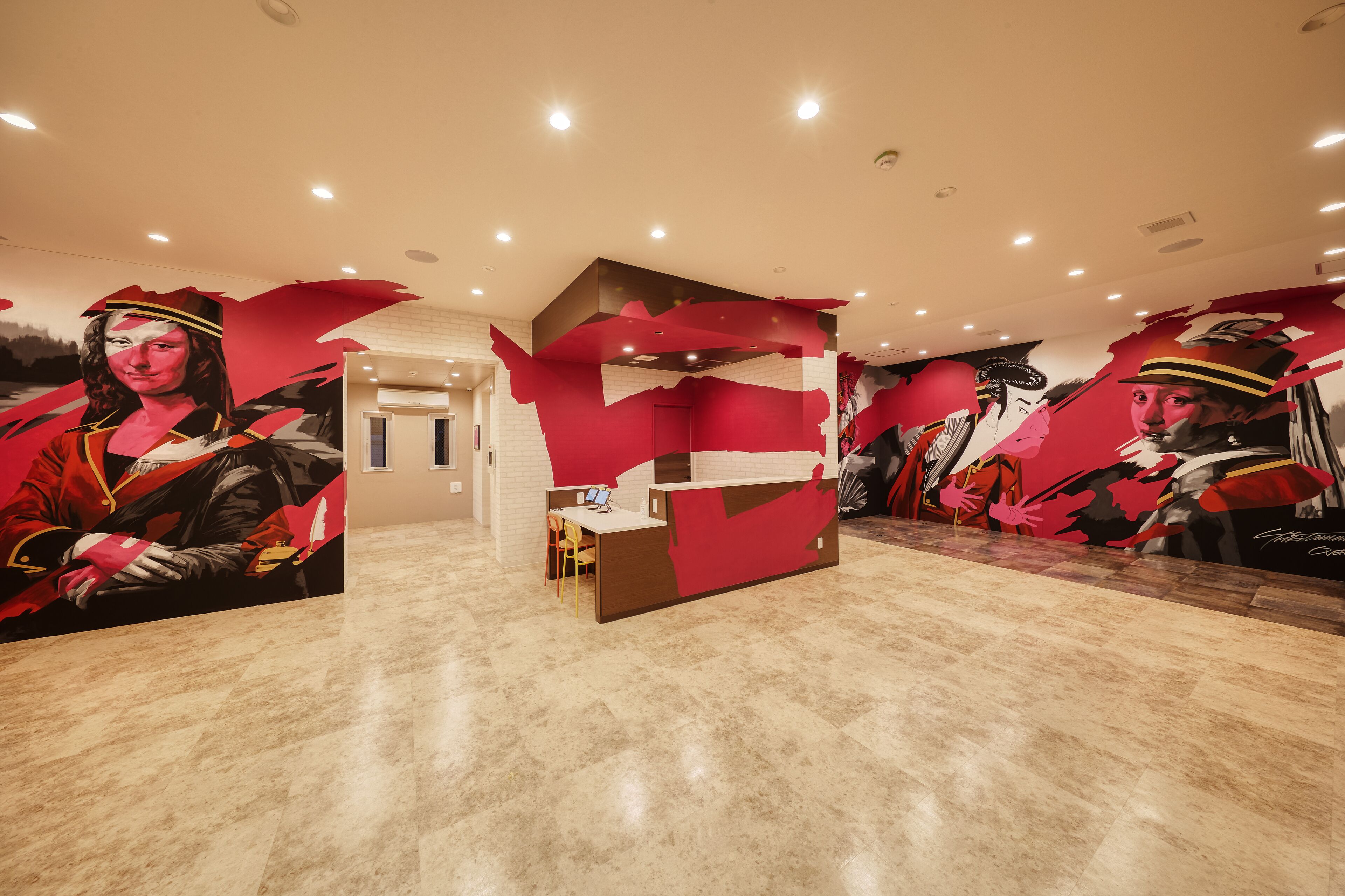 A modern hotel lobby with a reception desk, a seating area, and a large mural on the walls.