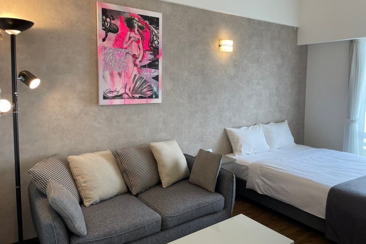 Quarto de hotel moderno com sofá cinzento, uma cama, uma obra de arte pendurada na parede e um abajur.