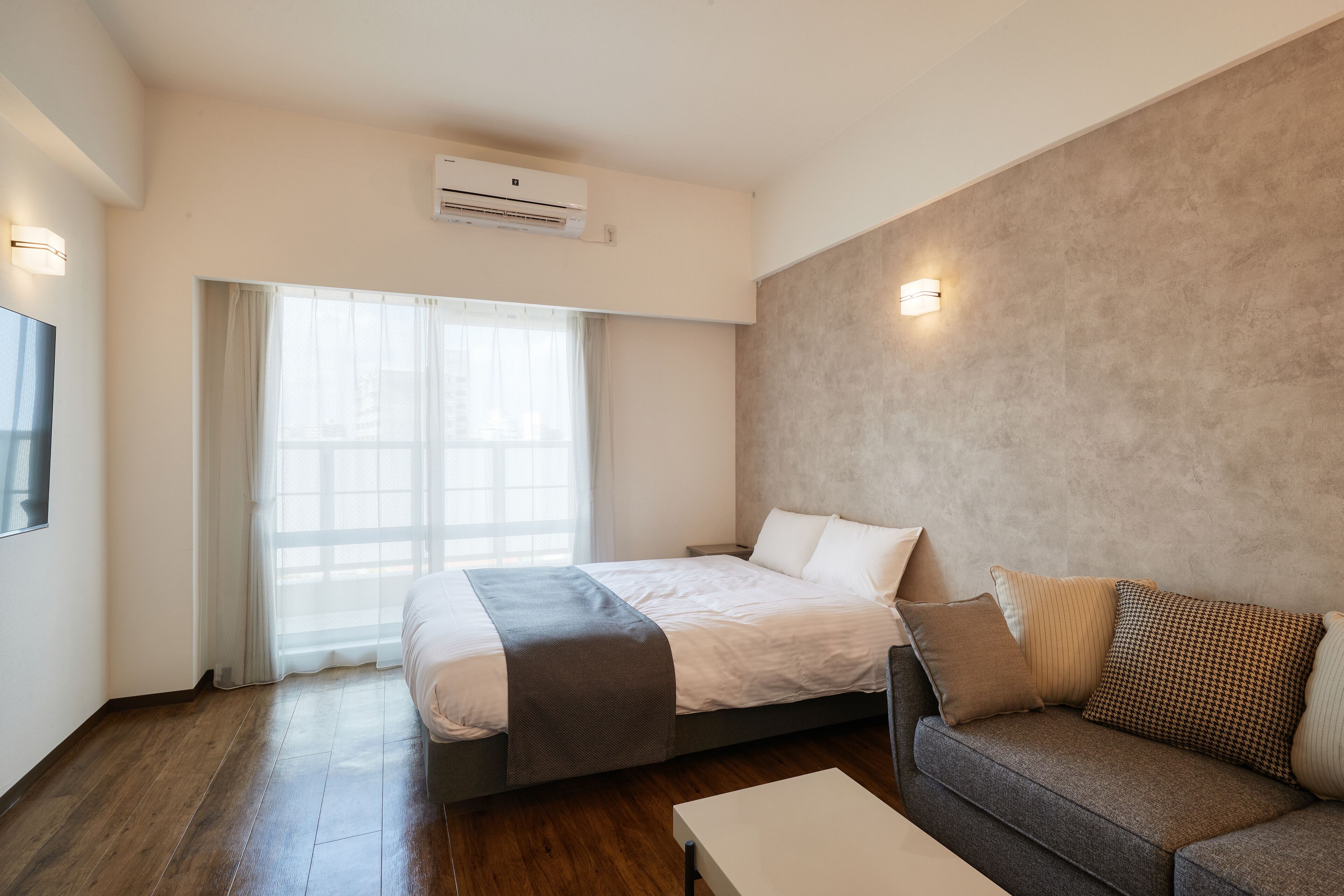 A modern hotel room with a bed, a sofa, a coffee table, and a large window with curtains.