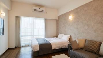 A modern hotel room with a bed, a sofa, a coffee table, and a large window with curtains.