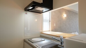 A compact kitchenette with a built-in oven, a sink, and a window providing natural light. - New Normal Hotel in NAMINOUE (Naha)