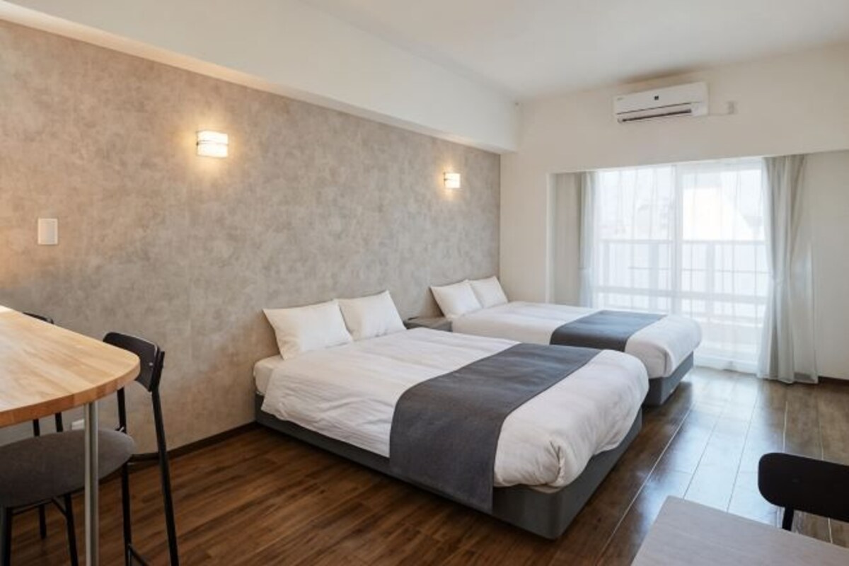 A hotel room with two beds, a dining table, and a window with curtains.