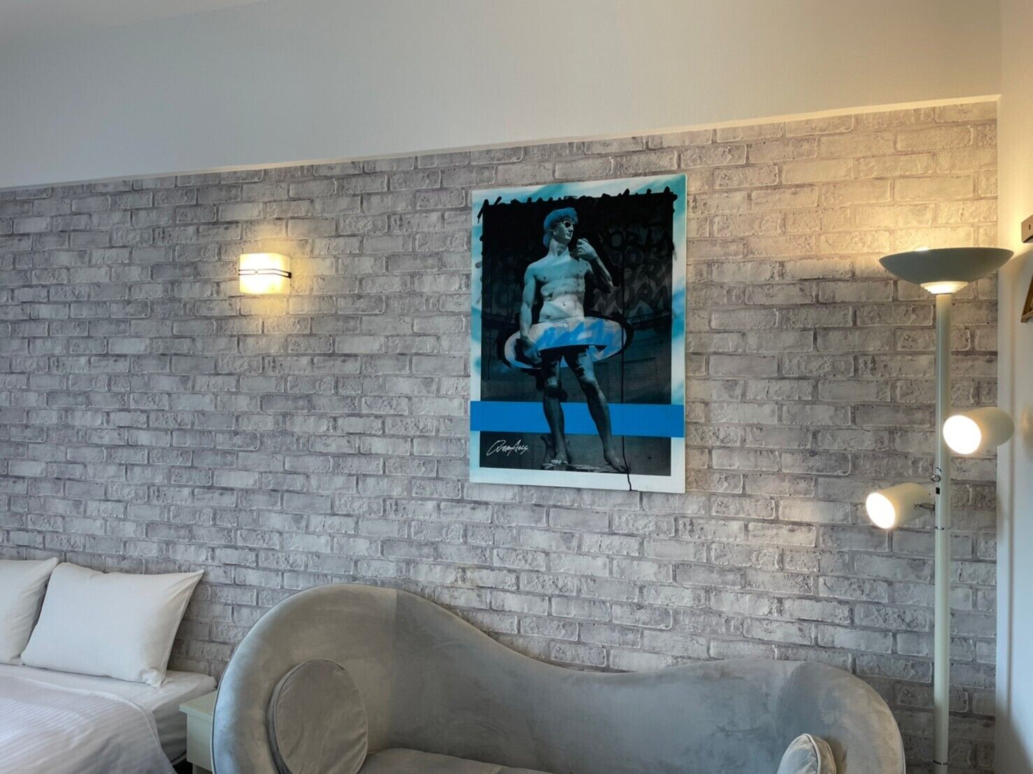 A room with a brick wall, a framed artwork, a sofa, and a lamp.