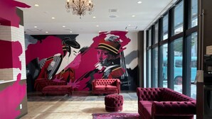 A modern lobby with a large mural, plush red furniture, and a chandelier. - New Normal Hotel in NAMINOUE (Naha)